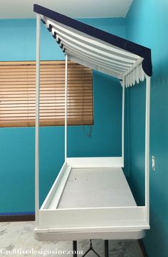 a canopy bed in the corner of a room with blue walls and wooden shutters