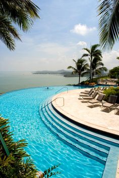 an empty swimming pool with lounge chairs and palm trees in the foreground, on a sunny day