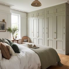 a bedroom with white walls and wood flooring is pictured in this image, the bed has many pillows on it