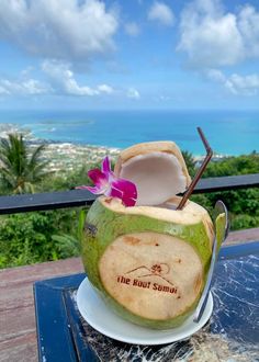 a coconut drink with a pink flower in it on a table overlooking the ocean and beach