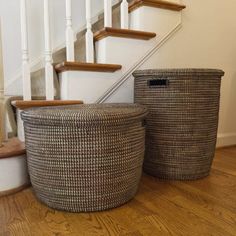 two baskets sitting next to each other on the floor in front of a stair case