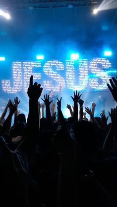 a crowd of people raising their hands up in front of a stage with the word jesus written on it