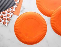 three orange paper plates sitting on top of a white table next to black and white papers