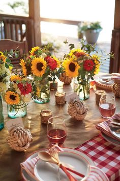 the table is set with sunflowers, pine cones and wine glasses on it