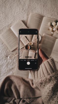 someone holding up their cell phone to take a photo with coffee and books on the table