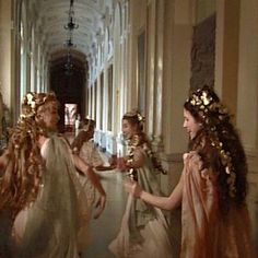 three women dressed in white dresses and gold hair are talking to each other on the hallway