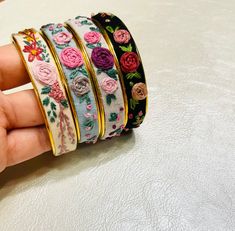 a hand is holding four different bracelets with flowers on them and gold trimming