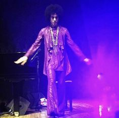 a man standing on top of a stage in front of a purple light with his hands out