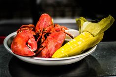 lobsters and corn on the cob are served in a white bowl with black countertop