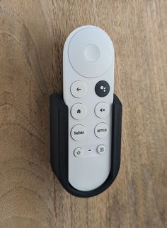 a white remote control sitting on top of a wooden table next to a black holder