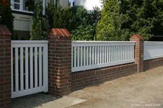 a white picket fence next to a brick wall