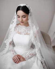 a woman in a white wedding dress sitting on a chair wearing a bridal veil