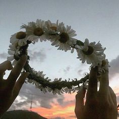 two hands are holding flowers in the shape of a circle as the sun goes down