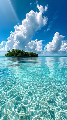 an island in the middle of the ocean under a blue sky with clouds above it