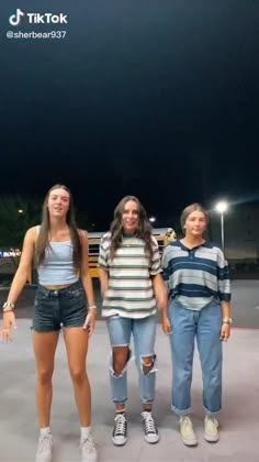 three young women standing next to each other in front of a school bus at night