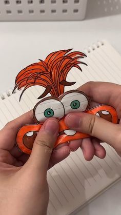 a hand holding an orange and white paper with a drawing of a cartoon character on it