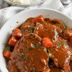 a bowl filled with meat and carrots covered in gravy on top of a table