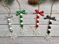 four christmas ornaments hanging from strings on a wooden table with pine cones and snowflakes