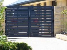 a large black gate is open in front of a house with trees and bushes around it