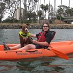 two people in an orange kayak with a dog sitting on the front and side