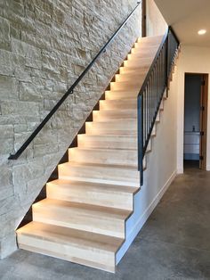 the stairs are made of wood and have black railings on each side, along with stone walls