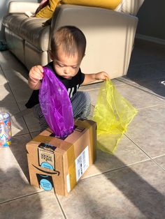 a little boy playing with a purple bag on the floor next to a cardboard box