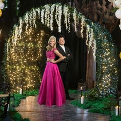 a man and woman posing for a photo in front of an archway decorated with lights