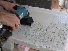 a person using a power tool on a piece of white paint with green and blue speckles