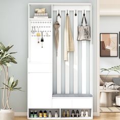 a white coat rack filled with coats next to a potted plant and pictures on the wall