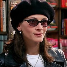 a woman wearing sunglasses and a hat in front of a book shelf with books on it