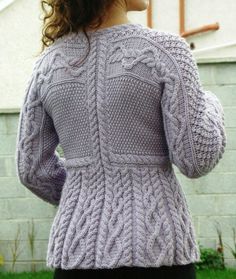 a woman standing in front of a house wearing a purple cabled sweater and black pants