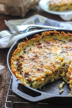 a quiche with cheese and other toppings in a cast iron skillet on a wooden table