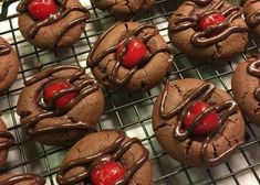 chocolate covered cookies with red cherries and drizzled in chocolate on a cooling rack