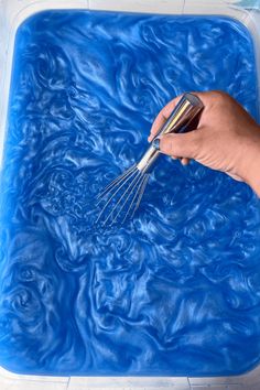 a person is using a whisk to mix blue liquid into a square container