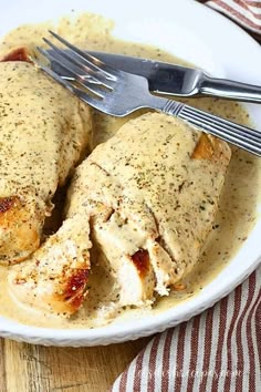 a white plate topped with chicken covered in gravy next to a knife and fork