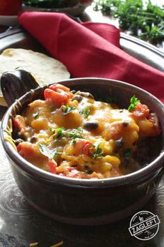 a close up of a bowl of food on a table with bread and vegetables in the background