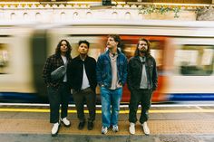 three men are standing in front of a train at a station with a blurry background