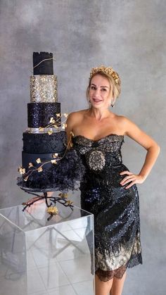 a woman standing next to a cake on top of a glass block wall in front of a gray background