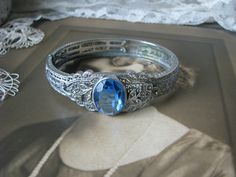 A beautiful Art Deco blue and clear paste floral filigree bangle bracelet. It measures 3/4'' at widest Measures 2 3/8'' x 2'' across the inside, and is 6 3/4'' along the inside. in very good condition with some graying and yellowing to the clear paste stones Wedding Filigree Bangle, Wedding Filigree Bangle Jewelry, Heirloom Wedding Bracelets With Intricate Design, Victorian Bangle Bracelets For Wedding, Victorian Bangle Bracelet For Wedding, Silver Filigree Bracelets For Wedding, Wedding Filigree Adjustable Bracelets, Wedding Filigree Bangle Bracelets, Adjustable Filigree Bracelets For Wedding