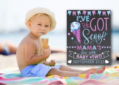 a little boy sitting on the beach eating an ice cream cone with a sign in front of him