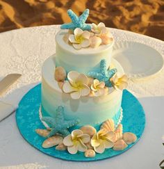 a three tiered cake with flowers and seashells on the top is sitting on a table