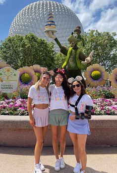 two girls standing next to each other in front of a flower garden with a large teddy bear statue behind them