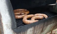 several sausages are cooking on an outdoor grill