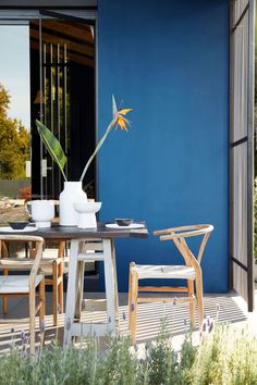 an outdoor table with chairs and a vase on it in front of a blue wall