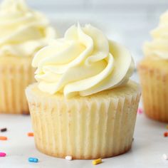 three cupcakes with white frosting and sprinkles on the table