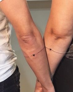 two people are holding hands with tattoos on their arms and one has a small heart