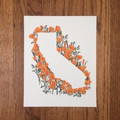 an orange flowered letter s on a white paper with wood grain flooring behind it