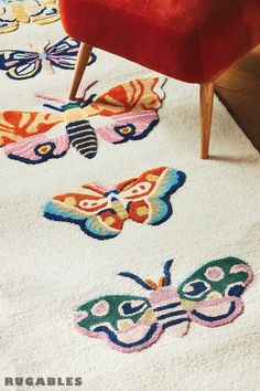 an area rug with butterflies on it in front of a red chair and wooden table