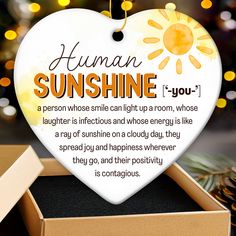 a white heart shaped ornament with the words human sunshine on it in front of a christmas tree