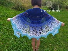 a woman wearing a blue crocheted shawl in the grass with her back to the camera